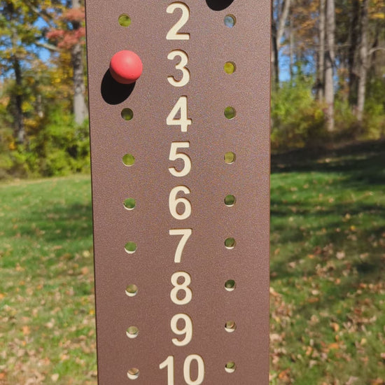 Outdoor demonstration of a brown bocce scoreboard with tan numbers and red and green scoring pegs.