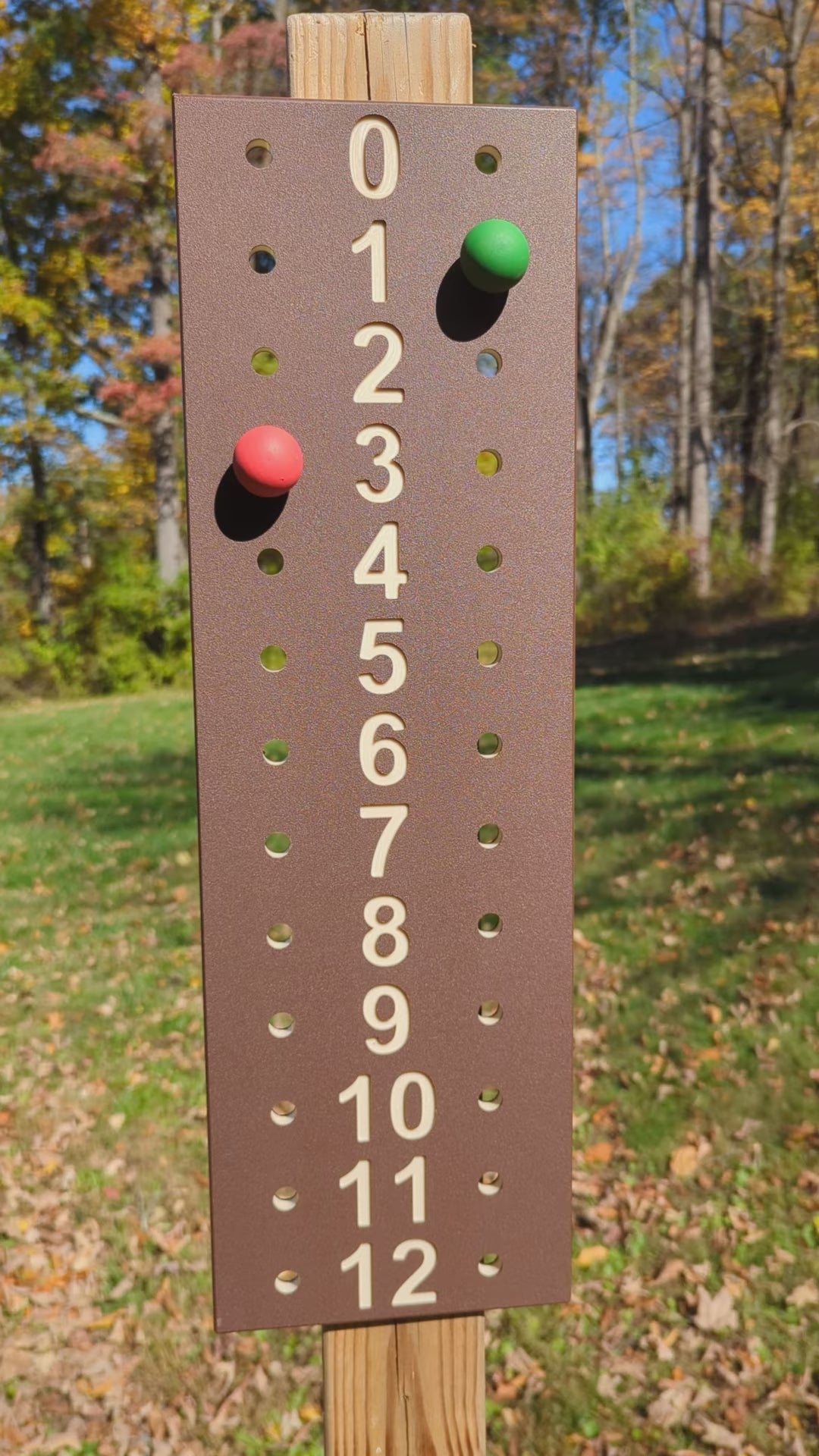 Outdoor demonstration of a brown bocce scoreboard with tan numbers and red and green scoring pegs.