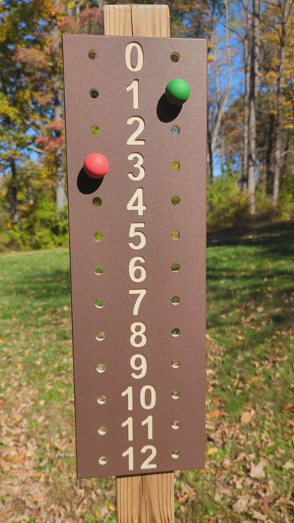 Outdoor demonstration of a brown bocce scoreboard with tan numbers and red and green scoring pegs.